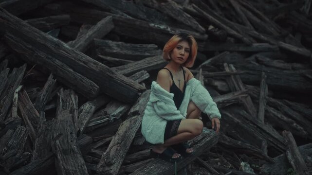 Young woman crouching on weathered driftwood in moody overcast light