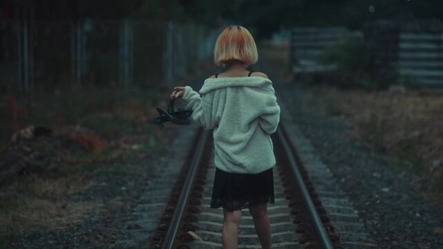 Young barefoot girl walking along railway tracks at dusk