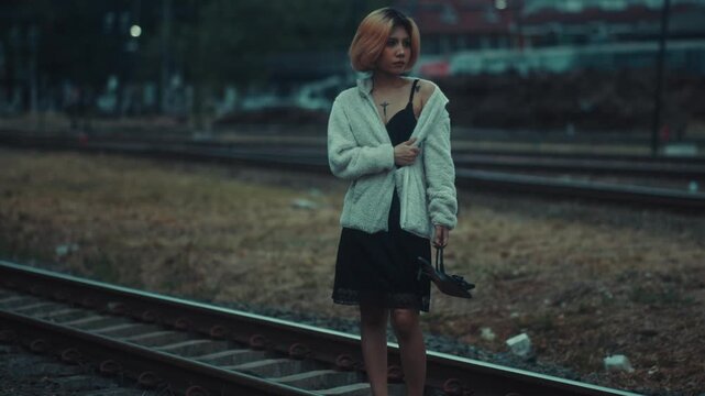 Young woman barefoot on railroad tracks at dusk