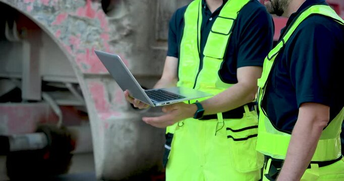 Close view of adult male logistics worker typing on laptop, updating cargo report, container inspection note, freight documentation, safety checklist near heavy truck equipment worksite zone
