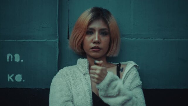 Young woman lighting a lighter against teal tiled train, moody close-up portrait