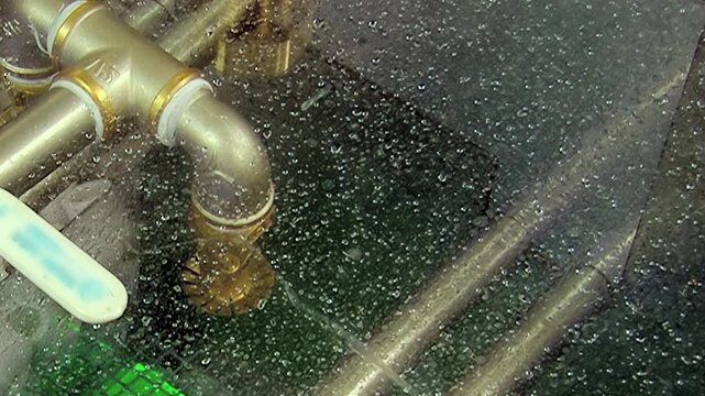 Intricate brass piping within hydro filter creates misty environment. Thousands water droplets cling to surfaces, signaling active air purification. Gentle emerald light glows from operational heart.