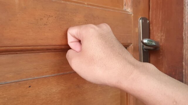 Close up of a guest hand knocking on a rustic brown timber door at daytime.
