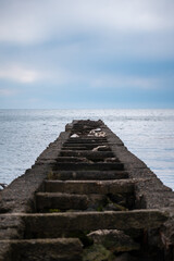 Obraz premium Old pier leading into calm water on a cloudy day