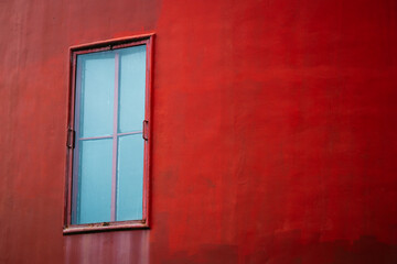 Fototapeta premium Red wall with a blue window in a simple setting during daylight hours