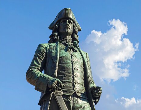 Bronze statue of a man in 18th-century attire under a blue sky with fluffy white clouds