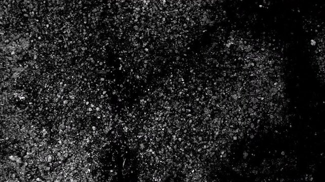 Dense granular texture resembling asphalt or stone, featuring scattered particles and shadowed areas