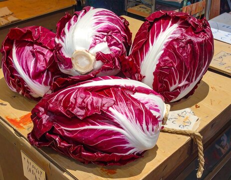 Close-up of four vibrant, burgundy-colored cabbages with white, crisp veins, arranged on a wooden surface in natural light