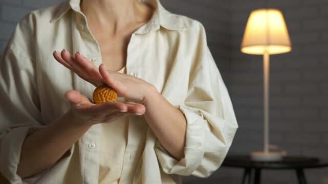 Woman massaging her hands with a spiky stress ball at home. Unrecognizable woman massaging her palms with a spiky sensory ball for hand therapy, stimulating acupressure points to relieve stress