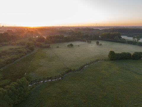 Diepenbeek, Belgium. Aerial drone view of misty agricultural landscape with sunrise and wind turbines on horizon