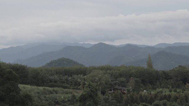 A beautiful morning timelapse of dark storm clouds moving over a vast mountain range and tropical green forest. Moody nature landscape.