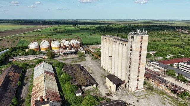 Aerial view of a large concrete grain elevator and industrial silos surrounded by green fields and rural landscape in Balchik, Dobrich Province, Bulgaria.