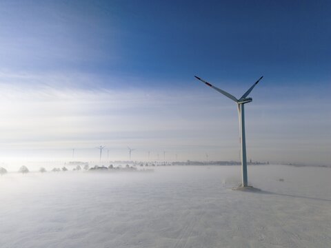 Wind turbine rises above foggy snow-covered landscape in clear blue sky, aerial view, wind turbine in snow in fog, between B&uuml;lten and Solschen, Ilsede, Peine district, Lower Saxony, Germany