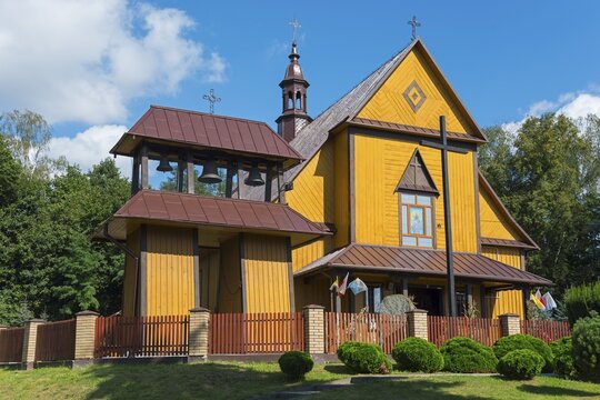 Yellow wooden church with bell tower and red roof, surrounded by trees and sky, Church of the Holy Apostles Peter and Paul, Olbięcin, Olbiecin, Powiat Kraśnik, Krasnik, Lublin Voivodeship, Poland