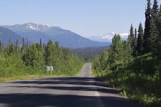 Narrow, traffic-free road leads as endless grades through rugged mountain landscape, forest and snow-covered mountains, wilderness, Stewart Cassiar Highway, British Columbia, Canada