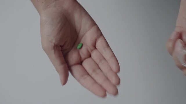 Hand Taking Green Pill from Small Glass Vial