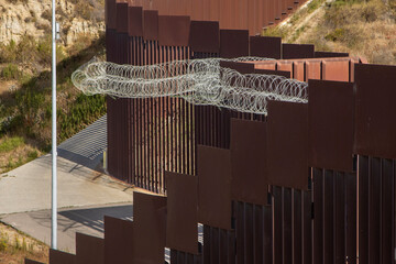 Looking down at the international boarder wall from Tijuana Mexico. There is silver coiled barbed wire © F Armstrong Photo