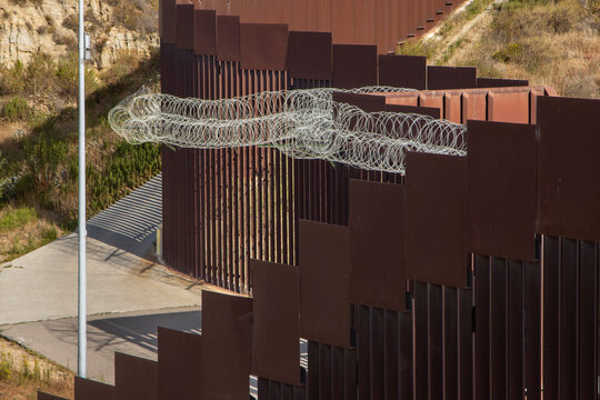 Looking down at the international boarder wall from Tijuana Mexico. There is silver coiled barbed wire