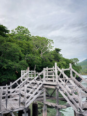 Fototapeta premium Wooden bridge pier over turquoise tropical sea with lush green forest and cloudy sky background