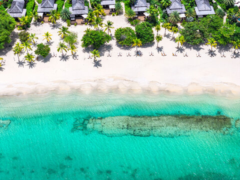 Aerial view of luxury beachfront villas and palm trees along a pristine white sand beach and turquoise water in English Harbour, Saint Paul, Antigua and Barbuda.