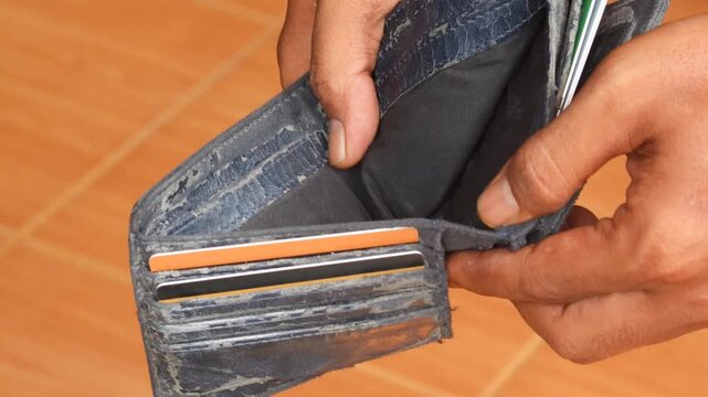 Close-up of Asian man opening an empty wallet with no money inside. Concept of financial stress, debt, poverty, economic crisis and personal money problems.