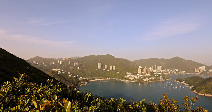 Hong Kong Repulse Bay panorama. Luxury apartments on lush green mountains. Calm blue sea with yachts. Clear sunny sky. High-end real estate meets tropical nature.