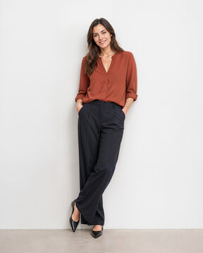 Smiling woman leaning against wall in rust blouse and black trousers