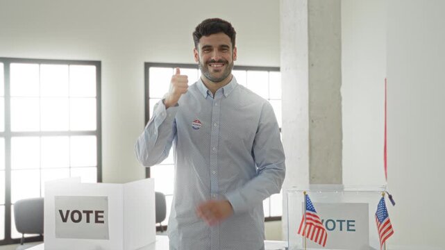 Man wearing an 'i voted' sticker giving thumbs up beside a ballot box with small american flags and a vote sign in a polling building; civic pride participation.
