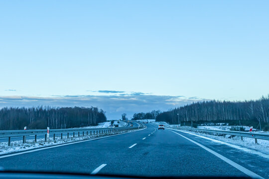 Modern Expressway Surrounded by Snow and Forest Beneath Blue Winter Sky. Clean roadway cutting through a snowy winter environment with forest visible in the distance.