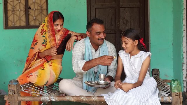 Indian family spending quality time together at village home, father feeds his young daughter while mother sitting nearby. care, bonding, and rural lifestyle