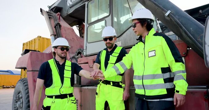 Adult male logistics team in PPE place hands together near reach stacker, celebrating slow motion yard teamwork, cargo handling safety, freight coordination, container dispatch commitment onsite