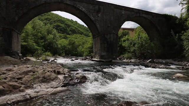 Flowing stream and ancient stone arched bridge from the 1700s, Modena Apennines, Italy, natural landscape