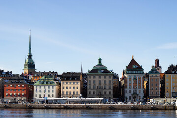 Obraz premium Colorful historic buildings line the waterfront in Stockholm, Sweden, showcasing architectural diversity with spires and domes against a clear blue sky