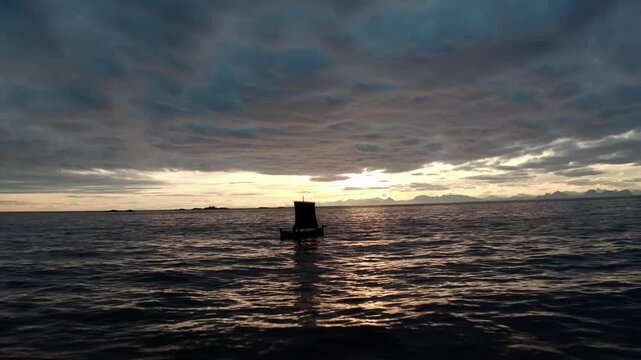 A Viking longship floats still in a calm ocean as the camera pulls back, showing distant mountains under a mostly cloudy sky with sunlight breaking through a cloud opening.