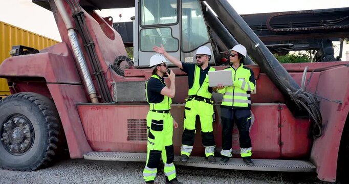 Adult Caucasian logistics group coordinate near reach stacker, using radio and laptop for freight operation, container handling safety, cargo dispatch, yard workflow and shipment control 