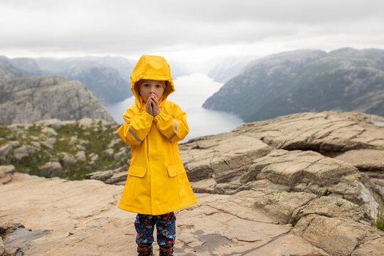 Family, enjoying the hike to Preikestolen, the Pulpit Rock in Lysebotn, Norway on a rainy day, toddler climbing with his pet dog the one of the most scenic fjords