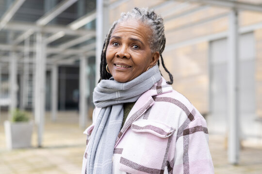 Senior African American woman standing and smiling in urban plaza wearing plaid coat and gray scarf