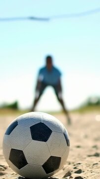 Vertical video: Camera focusing ball on sand, blurred man holding stance in blue preparing to block