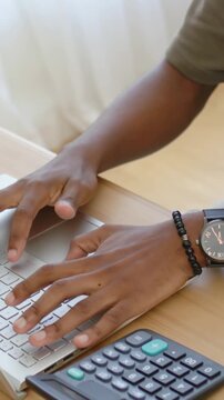 Vertical video: Hovering hands tapping keyboard at desk with calculator and shirt for data entry