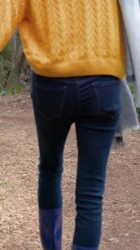Vertical video: Cam pulling back, woman walking holding hands fixing hat on path, purple boots