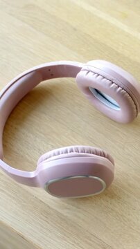 Vertical video: Panning camera revealing pink headphones on wood tabletop, showing cushioned pads