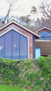 Vertical video: Tilting camera revealing wood-clad gabled facade on hill to show triangular window