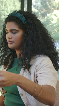 Vertical video: Feeling thirsty, woman in teal band and bangles lifting glass cup to sip by window