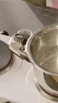 Vertical video: Reaching for pink crystals to season, cook shifting pan off hotplate on counter