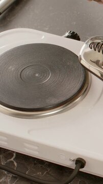 Vertical video: Pouring from glass cup hand filling steel pot on counter placing pot on hob to boil