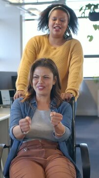 Vertical video: Pushing, woman in mustard knit guiding chair as peer miming driving at work for fun
