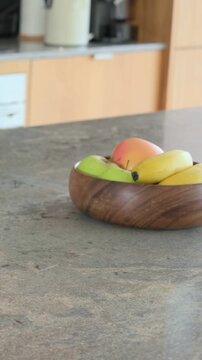 Vertical video: Panning camera toward wooden bowl on stone top with bananas apple peach, copy space