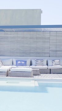 Vertical video: Shifting sunlight causing pool water rippling by wicker sofa with ottoman, pillows