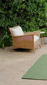 Vertical video: Starting pan camera revealing wicker chair, green mat and bottle on patio for yoga