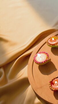 Vertical video: Lowering hands with beaded sleeve holding lit diya onto wood tray at table for puja